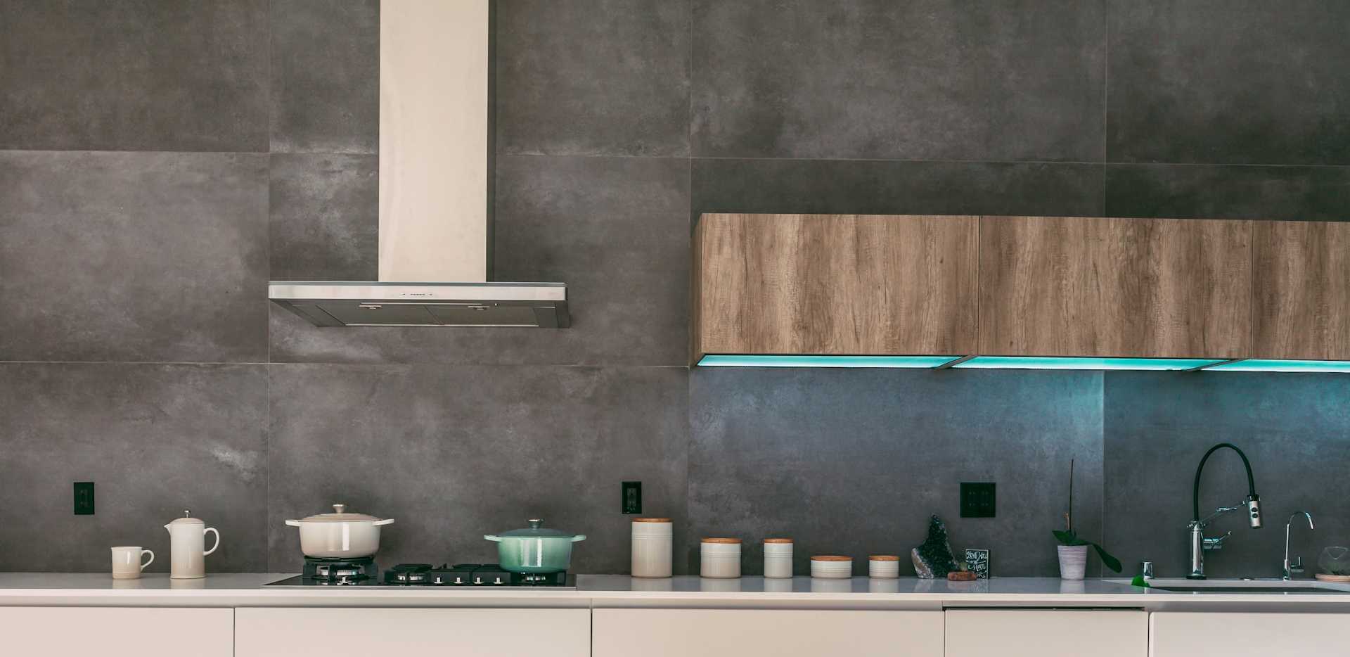Minimal kitchen with wood upper cabinets, gray surfaces, and an illuminated backsplash.