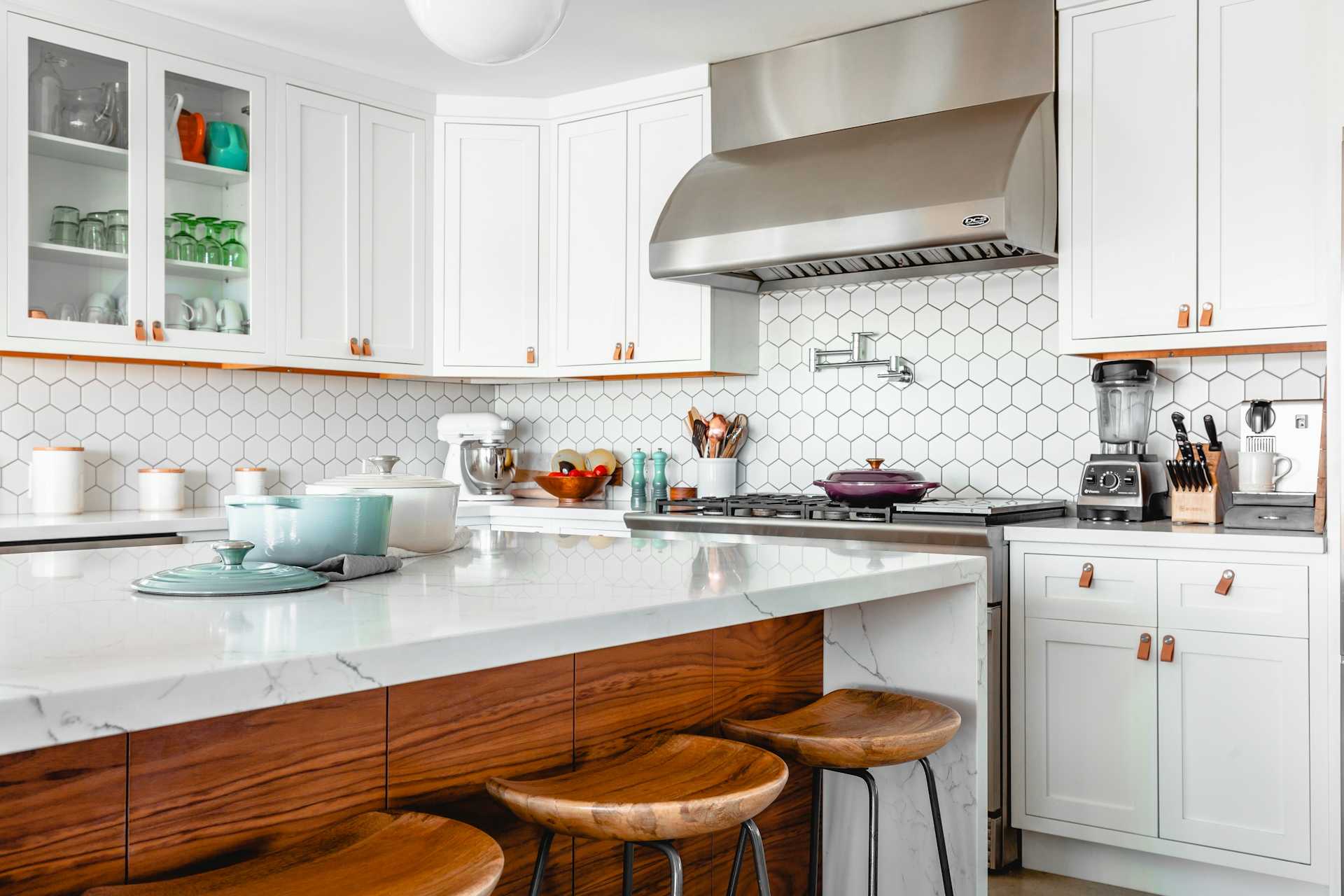 Bright kitchen with white cabinets, wood stools, and a patterned backsplash.