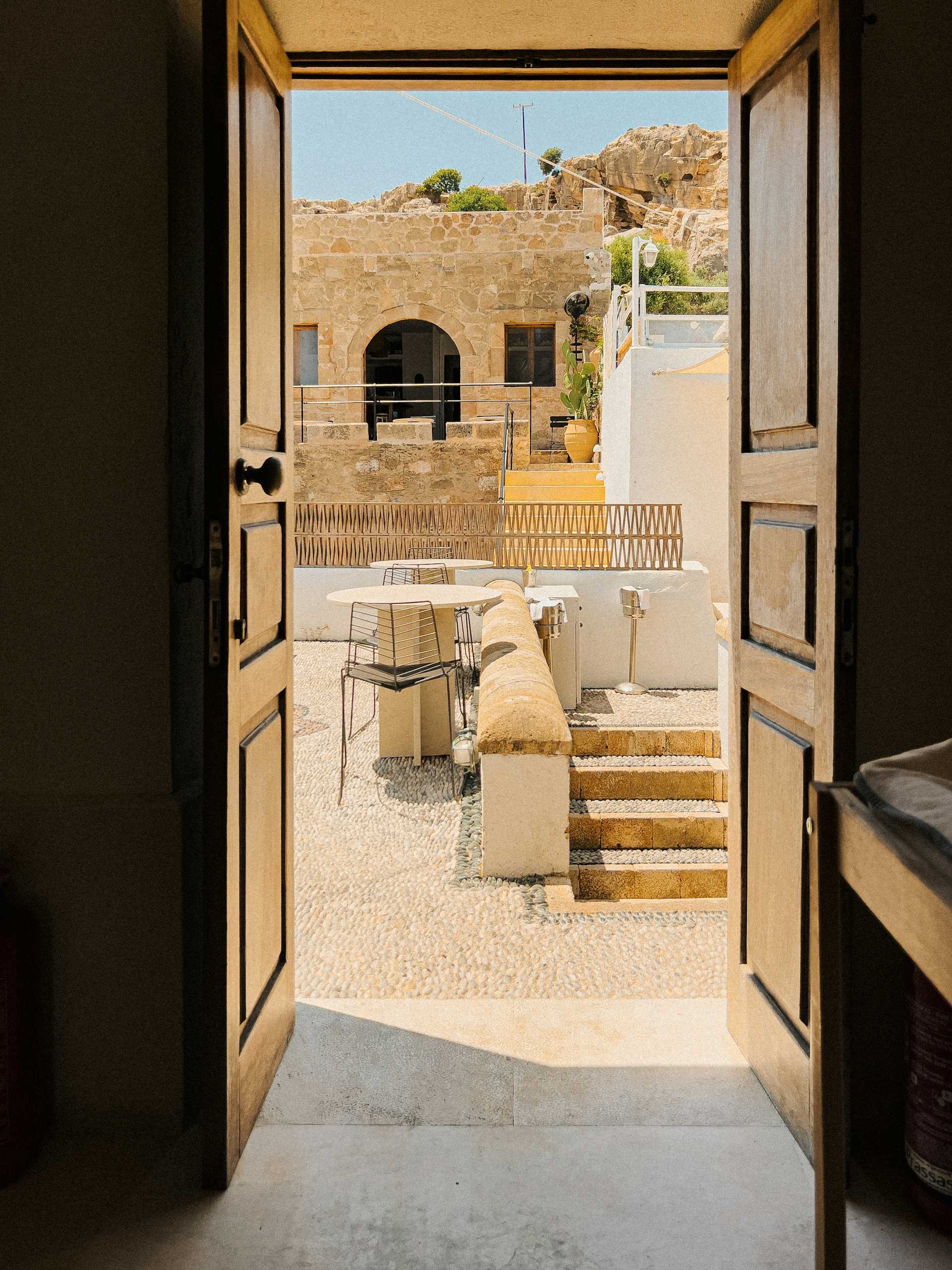 Wood doorway framing a sunlit stone courtyard in Lindos, Greece.