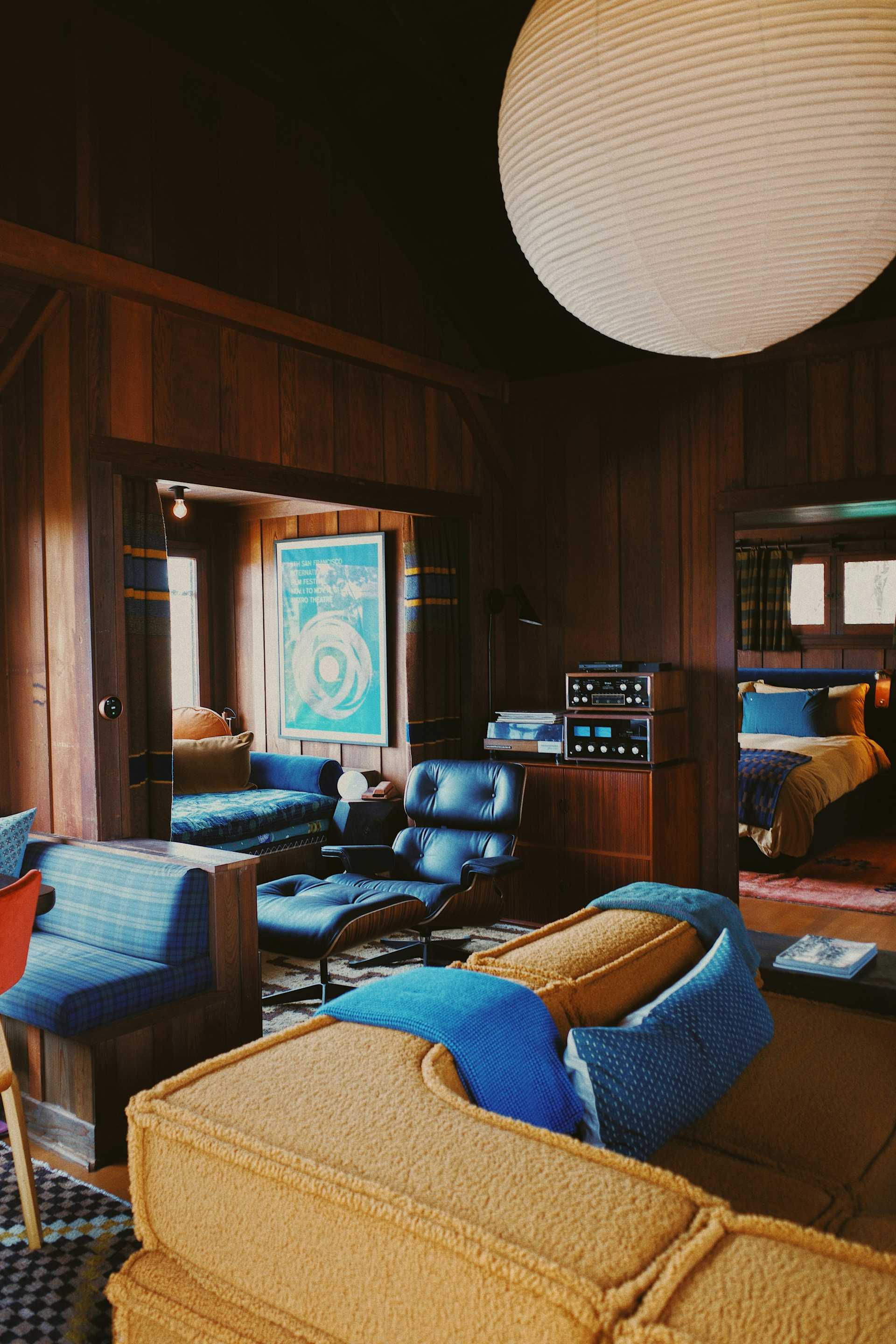 Wood-paneled room with a lounge chair, colorful seating, and a globe light.