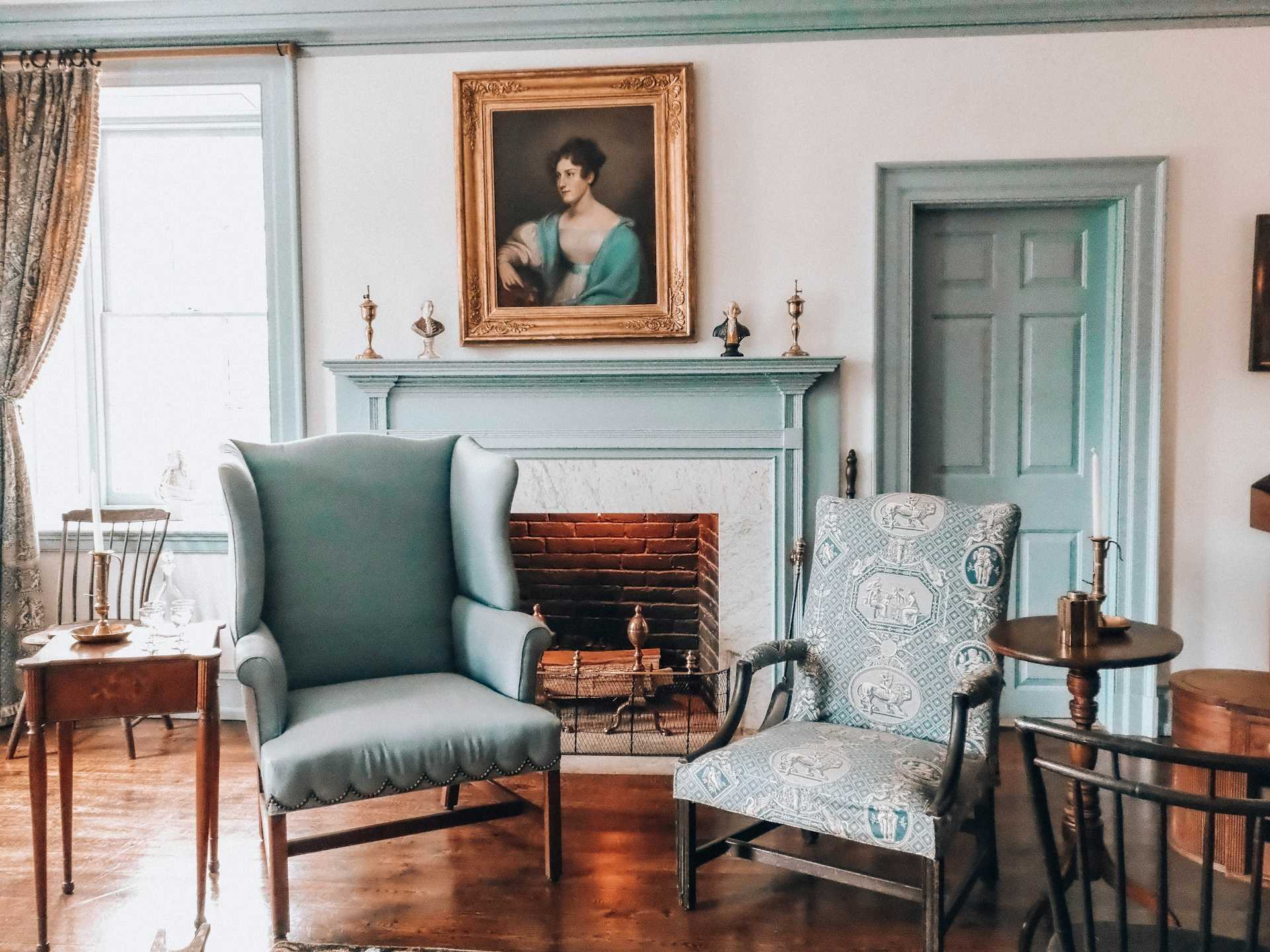 Two upholstered armchairs beside a painted mantel and a framed portrait.