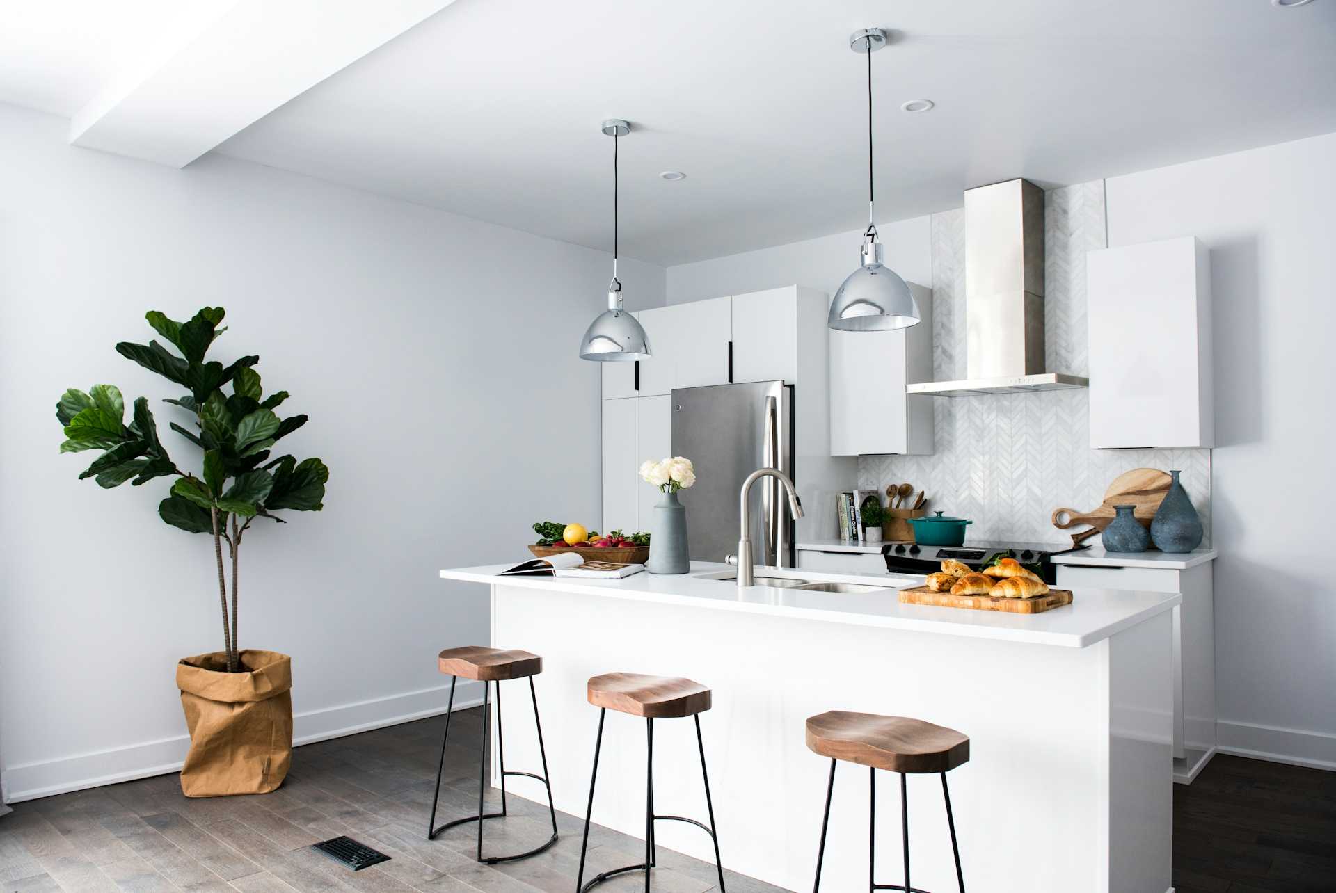 White kitchen with wood stools, gray pendant lights, and stainless appliances.